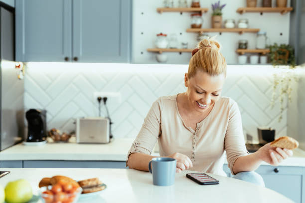 istock Mature woman enjoying time at home in kitchen with smart phone, using mobile app 1704292650