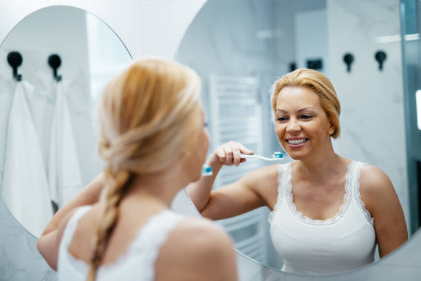 istock Cheerful mature woman in bathroom brushing teeth 1704292885