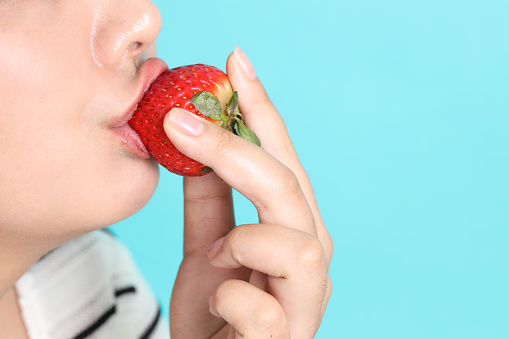 The Asian woman eating strawberry from the hand on the green background.