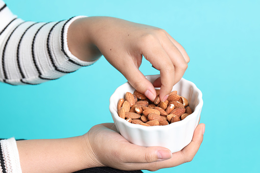 The Asian woman holding almond nut in the hand on the green background.