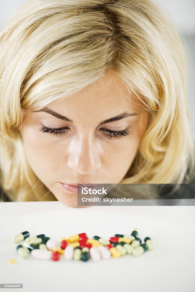 Beautiful blonde woman is looking at the pile of pills. Close-up of a serious female looking at the tablets. Addiction Stock Photo