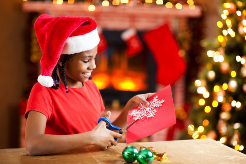 Cute African-American girl wearing Santa's hat is making Christmas card.   