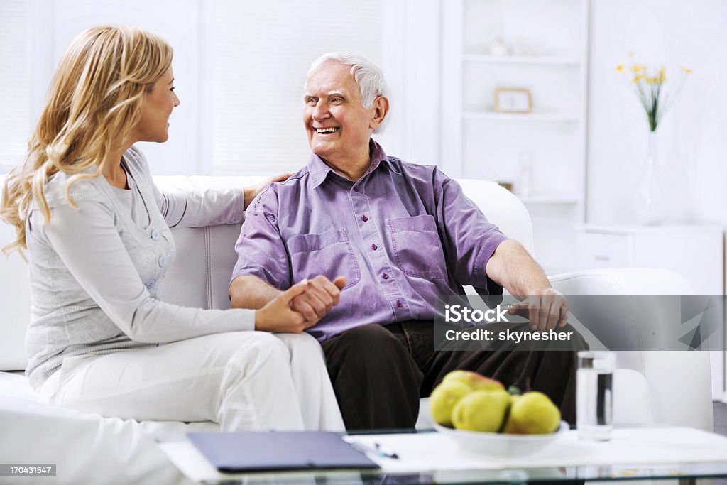 Home caregiver sitting n the sofa with an elderly man Cheerful woman sitting on the sofa with a senior man and holding his hand.    Senior Adult Stock Photo