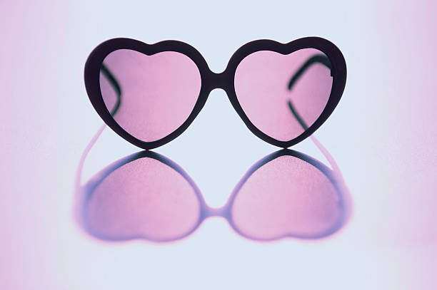 Rose Colored Glasses Sit on Reflective Background Rose colored heart shaped glasses sit on reflective grainy formica background shot with pink filter to give a romantic hue tinted sunglasses stock pictures, royalty-free photos & images