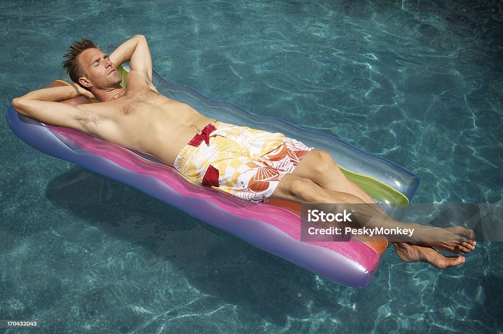 Uomo si rilassa sul materasso di aria in piscina colorato - Foto stock royalty-free di Dormire