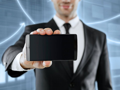 Businessman holding a mobile phone with blank screen in front of a digital board