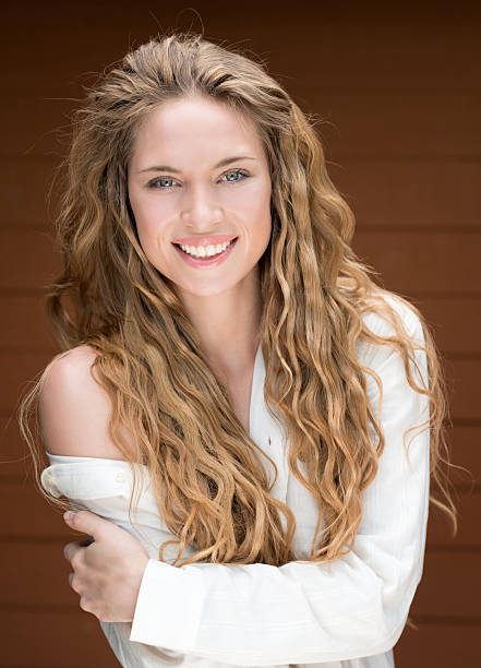 A young woman in her early 20s leans against a sleek, modern glass fence, smiling happily and gazing up at the sky. The contrast between her joyful expression, the contemporary glass fence, and the antique stone background creates a harmonious blend of old and new. With ample copy space around her, this image captures a moment of peace, contentment, and reflection during her city break. Perfect for use in lifestyle blogs, travel content, or marketing materials promoting city tourism, outdoor adventures, or modern architecture. Ideal for promoting a sense of joy, exploration, or cultural fusion, and great for content that celebrates personal moments, modern cityscapes, or wellness. Ideal for advertising products or services related to travel, photography, or modern living.