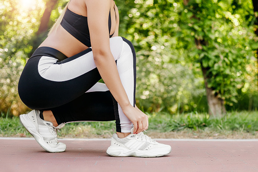 Close up of young woman getting ready for jogging outdoors while lacing her sneakers. Health and sport concept. side view