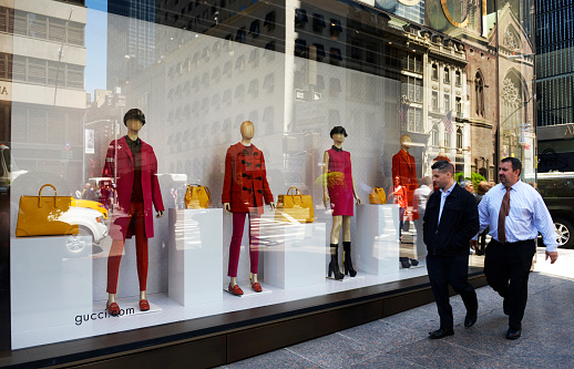 New York City, USA - May 30rd 2014: Two businessmen walking in front of Gucci store.  Gucci is an Italian fashion and leather goods brand founded by Guccio Gucci in Florence in 1921.