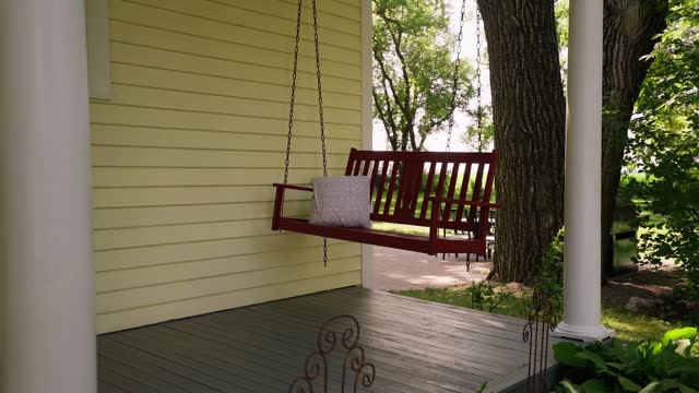 orbiting shot of a red hanging swing on the front deck of a farmhouse
