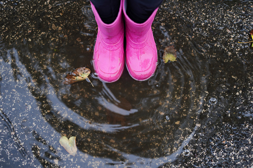 Child wearing pink rain boots staying into a puddle with yellow leaves , autumn season