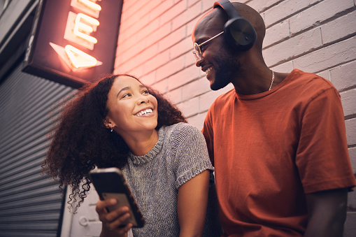 Phone, music and headphones with an interracial couple outdoor in a city together for dating. Love, mobile app or streaming with a man and woman bonding in an urban town while listening to the radio