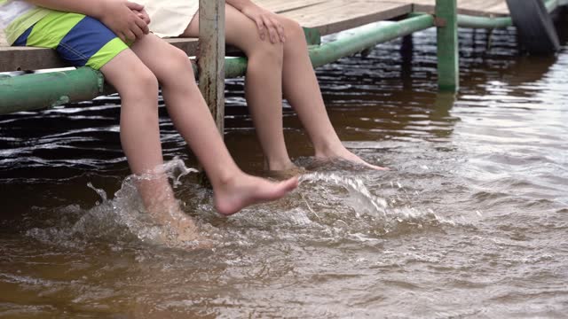 children dangle their feet in the water of the lake sitting on the pier