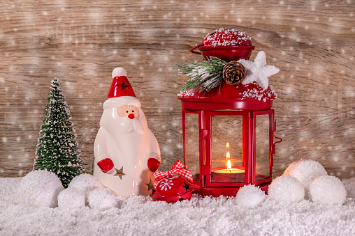 Christmas red lantern, decorative Santa Claus, Christmas tree and bell in the snow. New Year's decor. Brown background.