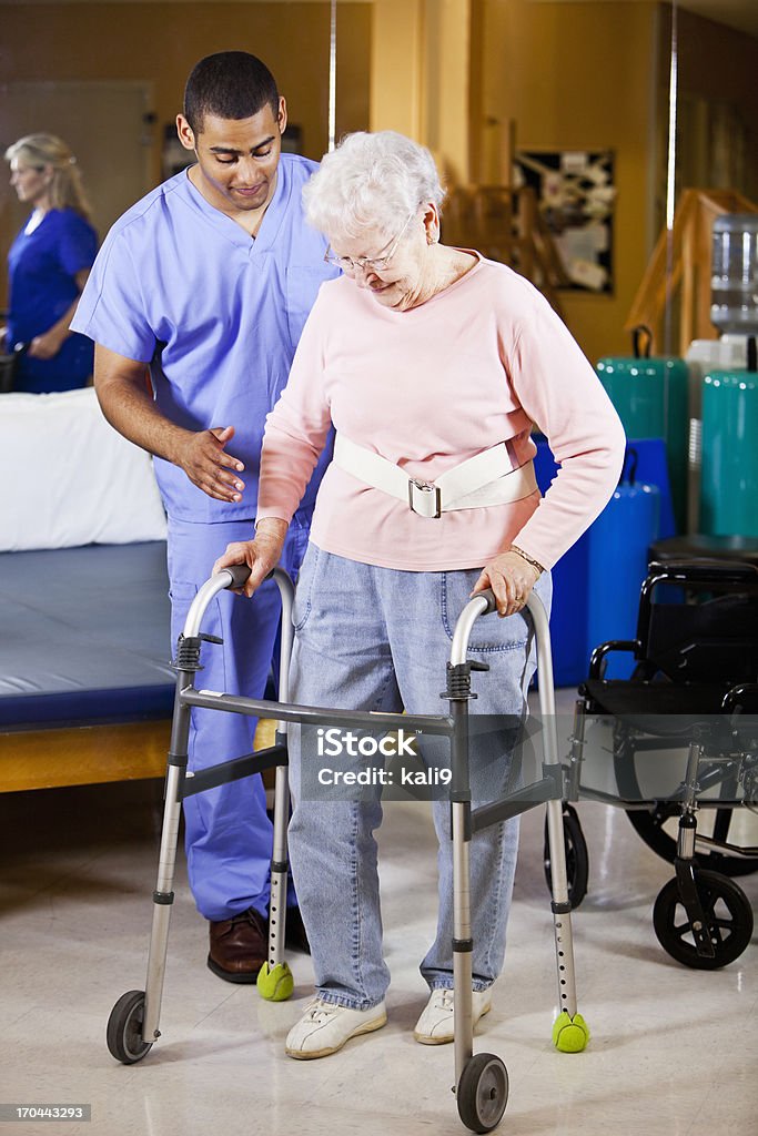 Personale sanitario aiutando senior donna utilizzare walker - Foto stock royalty-free di Terapia occupazionale