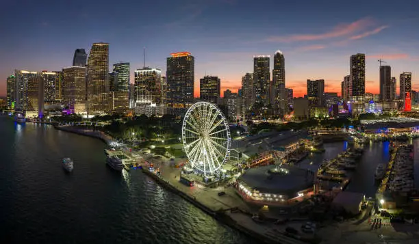 Photo of High illuminated skyscrapers of Brickell, city's financial center. Skyviews Miami Observation Wheel at Bayside Marketplace with reflections in Biscayne Bay water and US urban landscape at night