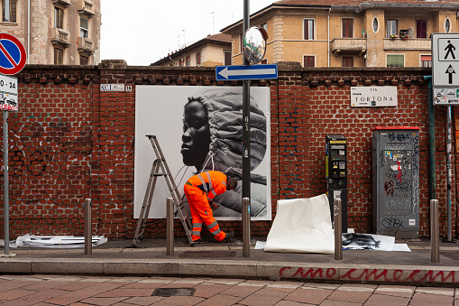 Milan, Italy - April 21, 2023: Workers are putting up posters showcasing the Moncler collection of 2023 on the walls