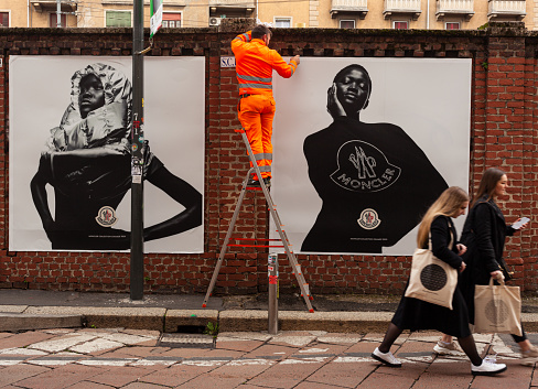 Milan, Italy - April 21, 2023: Workers are putting up posters showcasing the Moncler collection of 2023 on the walls