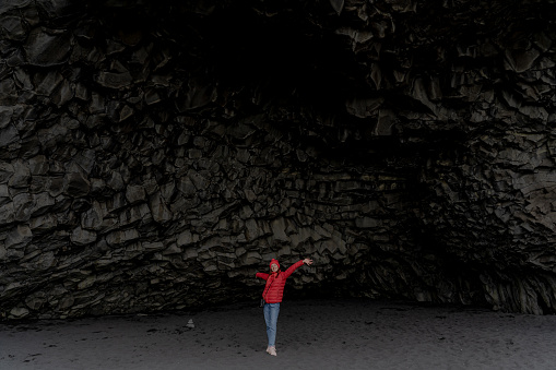 A girl poses in a cave on a black beach. Black beach in Vik. Iceland.