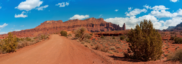 Panoramic view of a sandy dirt road leading towards Fisher Towers near Moab, Utah, USA.