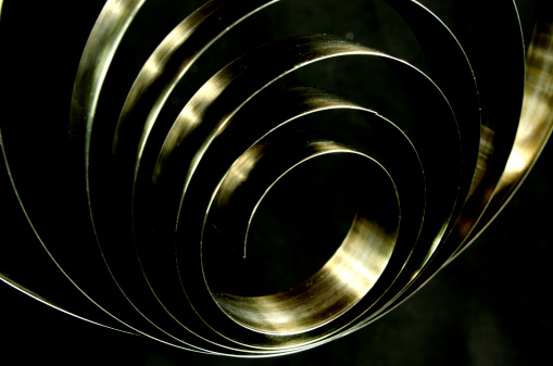 A brass  band spring from a 150 year old clock. On a black background with some copy space. Selective focus on the center of the spring.