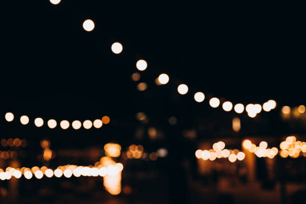istock Decorative string lights at night time, Defocused Background, night city life backdrop, party time with Yellow bokeh balls. Warm festive bokeh of string lights over an outdoor bar or patio at twilight 1704567522