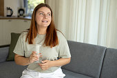 Young woman drinking pure water from glass and sitting on textile couch at home. Health care concept photo, lifestyle, close up