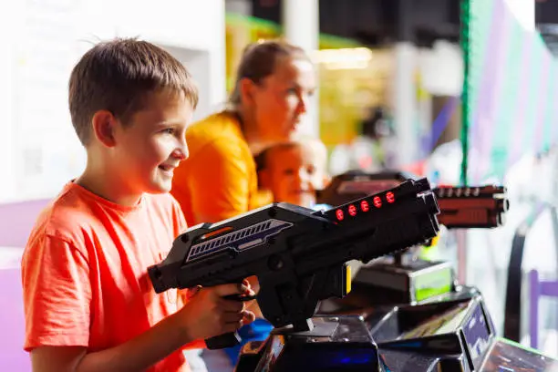 Happy kids playing a shooting game on slot machines at an amusement park.