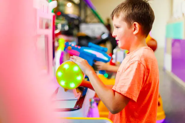 Happy kid playing fun games on arcade machine at an amusement park.