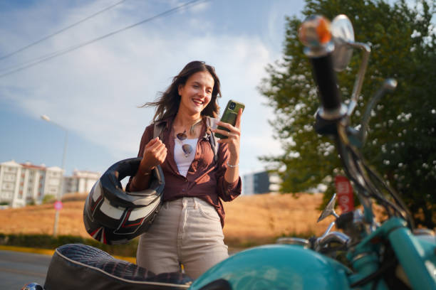 Young female driver using mobile phone next to her motorbike.
