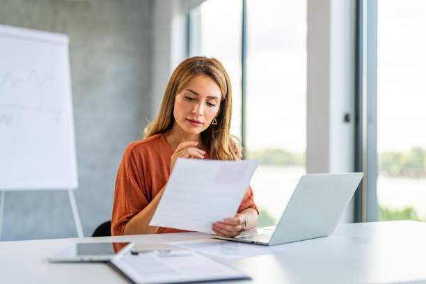 Young happy and successful businesswoman working with documents inside office. Business woman busy working on laptop computer at office paperwork stock pictures, royalty-free photos & images