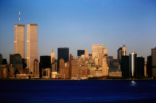 In the tranquil midst of the sea, a mesmerizing tableau unfolds. Manhattan's iconic skyline, adorned in the warm embrace of a setting sun, features the World Trade Center's twin towers, symbols of urban majesty.