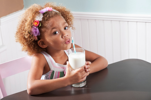 Cute little girl (4 years, mixed race), sitting at table with glass of milk.