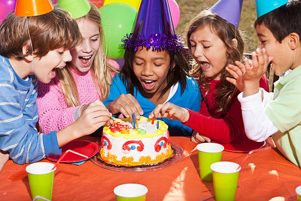 Multi-ethnic children (7-10 years) having fun at birthday party, taking candles off birthday cake.
