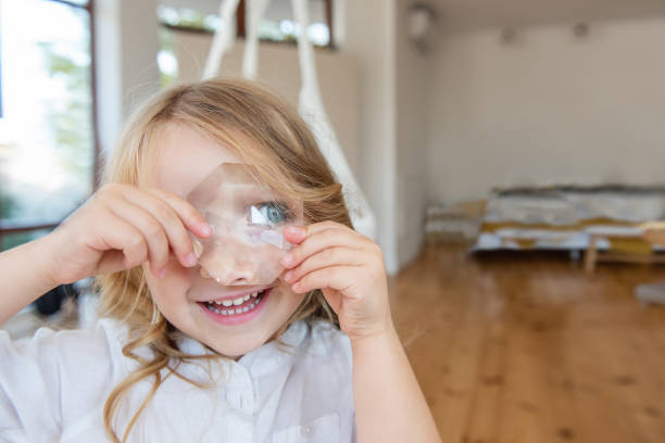 portrait en gros plan d’une petite fille blonde tenant une loupe en cristal brillant à l’œil. - child blank expression pensive focus on foreground photos et images de collection