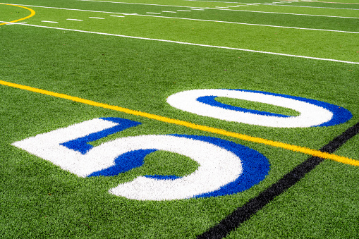 Synthetic turf football 50 yard line in white with royal blue shadow along with black lacrosse line and yellow soccer mid field line