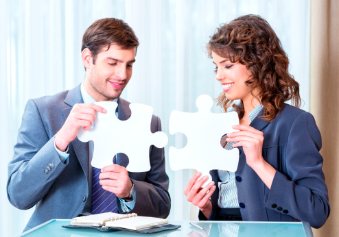 Young business people stitching two pieces of jigsaw puzzle