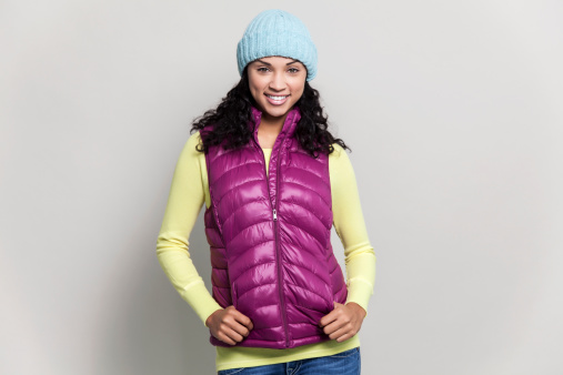 Beautiful mixed race woman with black curly hair wearing a blue winter hat, purple scarf, purple vest and yellow sweater. The model has pretty green eyes, and a beautiful smile.