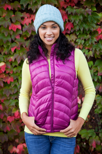 Beautiful mixed race woman with black curly hair wearing a blue winter hat, purple scarf, purple vest and yellow sweater. The model has pretty green eyes, and a beautiful smile.