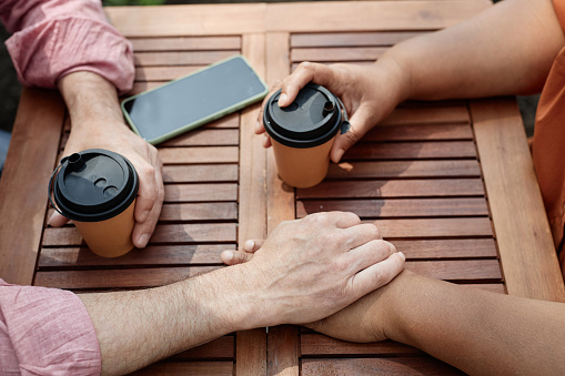 Top view closeup of two senior people holding hands while enjoying romantic date at outdoor cafe