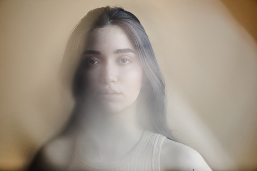 Blurred portrait of young woman struggling with mental health issues and looking at camera