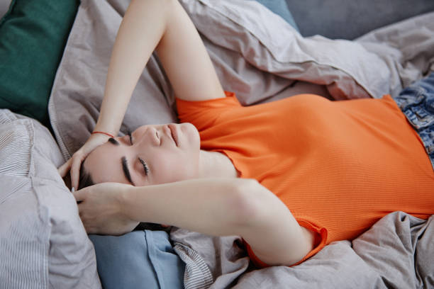 朝ベッドに横たわり、うつ病に苦しんでいる高角度の悲しい若い女性 - 仰向きに寝る ストックフォトと画像