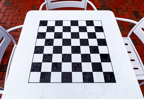 Close-up of rain-splattered whtie metal table with a black and white chess and checkers board.