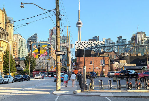 Toronto, Canada - August 22, 2023: Two pedestrians walk south on McCaul Street near Darcy Street in the Kensington-Chinatown neighborhood. The CN Tower stands in the background. Summer early evening with a clear sky.