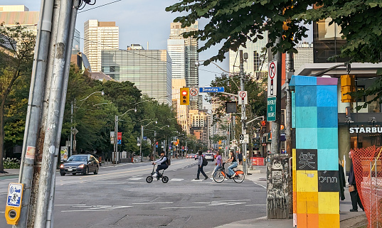 Toronto, Canada - August 22, 2023: Cyclists and pedestrians cross College Street at Beverley Street near the University of Toronto campus. Education and commercial buildings line College Street in the Toronto Discovery District.