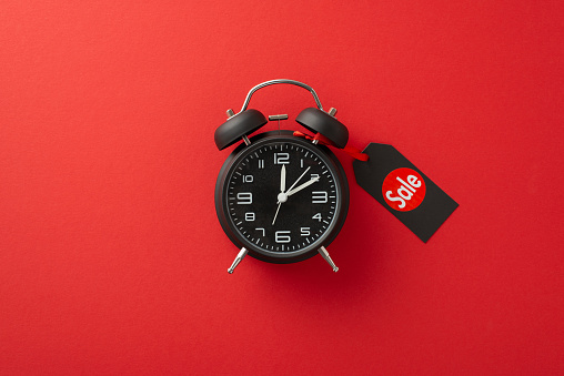 Tick-tock, Black Friday o'clock! A top view image of black alarm clock adorned with a 'sale' price tag on a red background, creating space for promotional text or advertisements