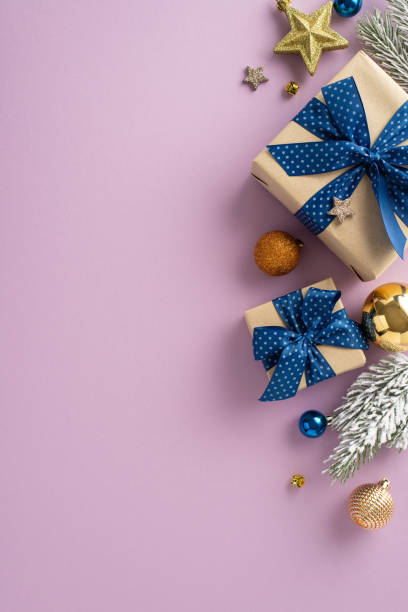 istock Festive wonderland: vertical top view of elegantly wrapped presents, chic tree ornaments, baubles set, sparkling stars, frosted fir branches on a lavender surface, with room for your festive greeting 1704730214