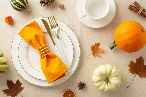 Captured from above, a fall-themed Thanksgiving family dinner with gilded plates, elegant cutlery, and autumnal decorations on beige tablecloth on table, offering space for text or advertisements