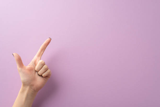 istock Young woman's hand, adorned with sleek black nails, forming pistol gesture using her index and thumb fingers. Captured from first person top view on lilac surface, providing space for text or ads 1704730805
