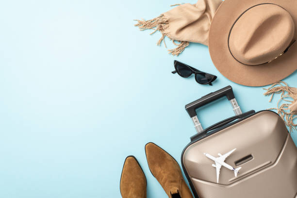 Elevate your fall vacation with elegance. Overhead shot captures a gray suitcase, soft scarf, chic boots and felt hat on light blue background, providing room for your advertising or textual content